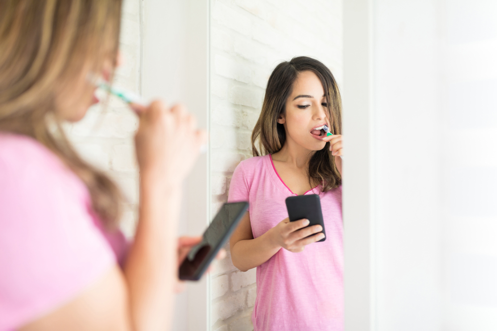 New Dental Apps Encourage Hygiene 1 Woman brushing teeth while looking at her phone